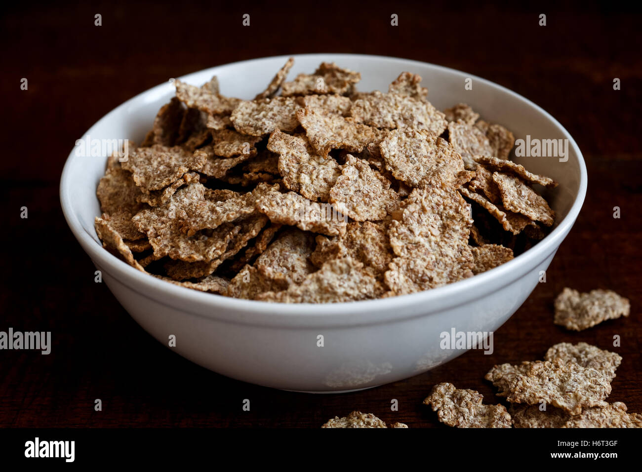 Wheat bran breakfast cereal with no milk in ceramic bowl. Moody lighting on  dark rustic wood surface. Spilt flakes next to bowl Stock Photo - Alamy