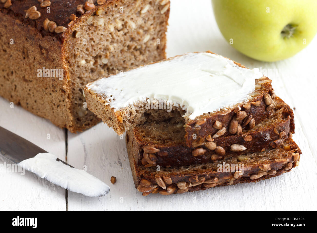 Sunflower seed loaf sliced, cream cheese spread, rustic surface, apple