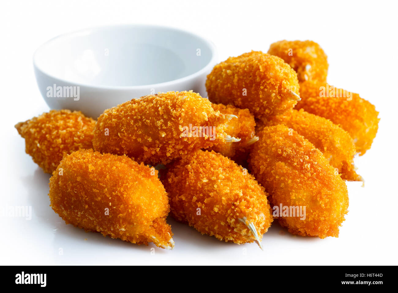 Pile of fried breaded surimi crab claws with empty dip bowl isolated on white. Stock Photo