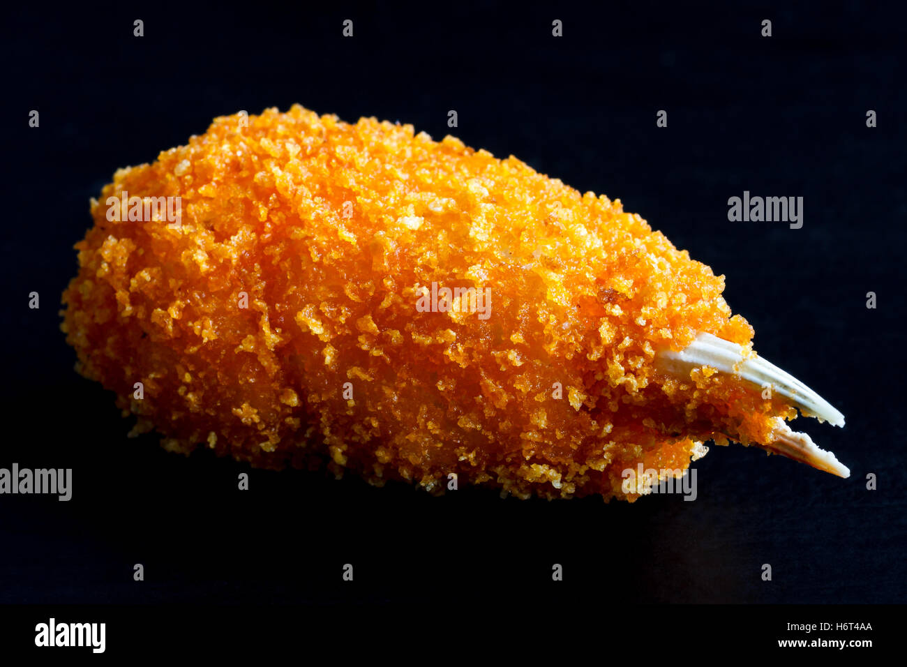 Detail of a fried breaded surimi crab claw isolated on black in perspective. Stock Photo