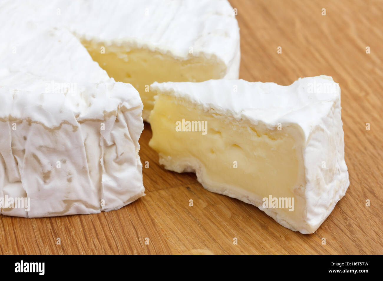Slice of white cheese cut out of a big round on a wood surface. Stock Photo