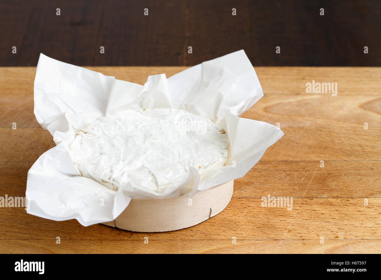 Whole white mould cheese in wrapping on wood board. Stock Photo