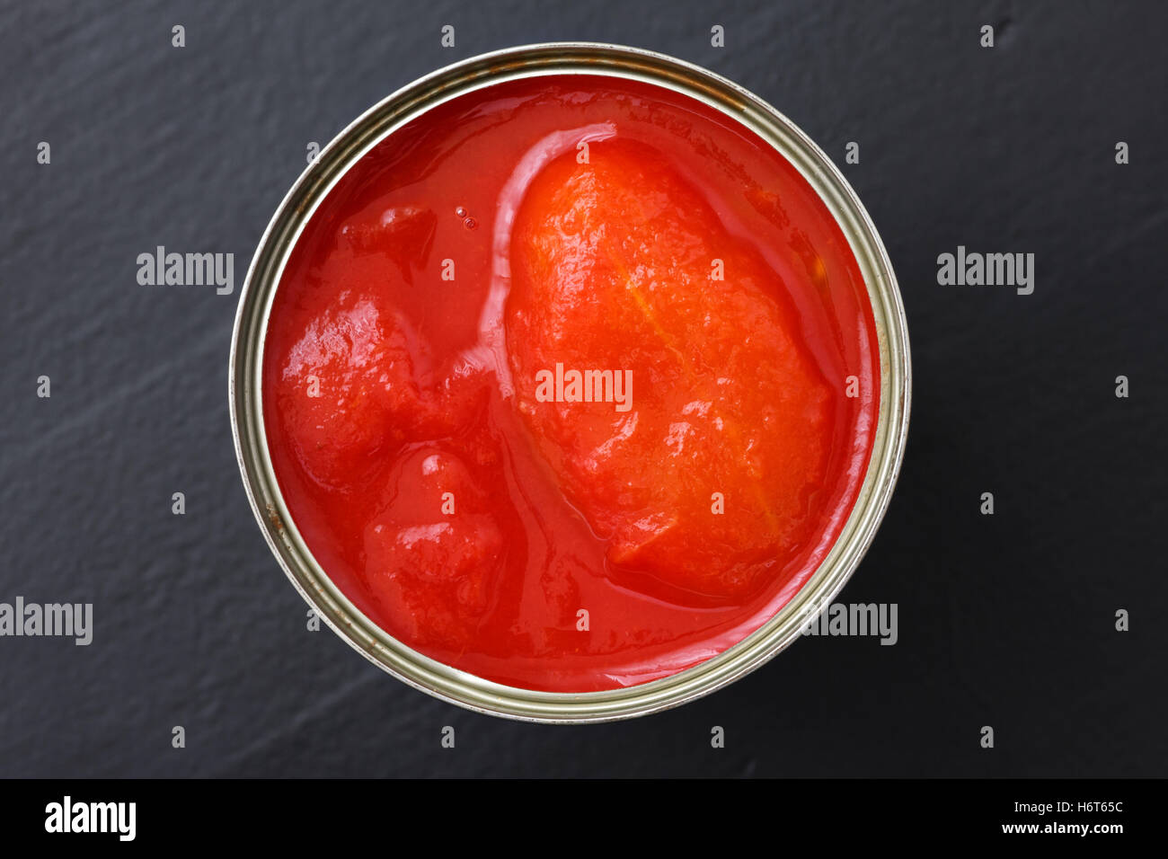 Whole canned tomatoes from above on black wood. Stock Photo