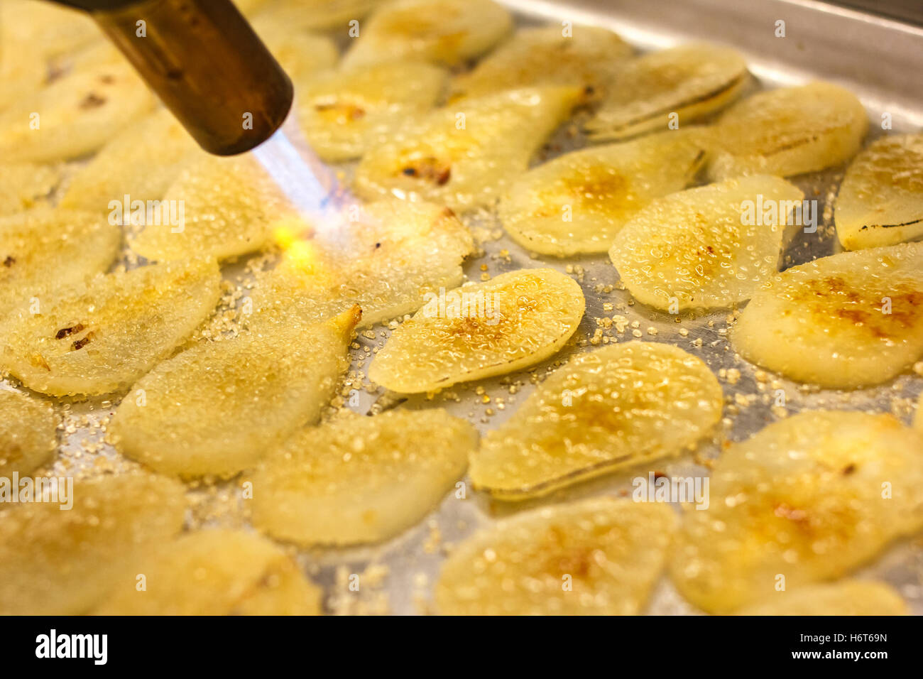 Blowtorch caramelising sugar on pear slices. Stock Photo