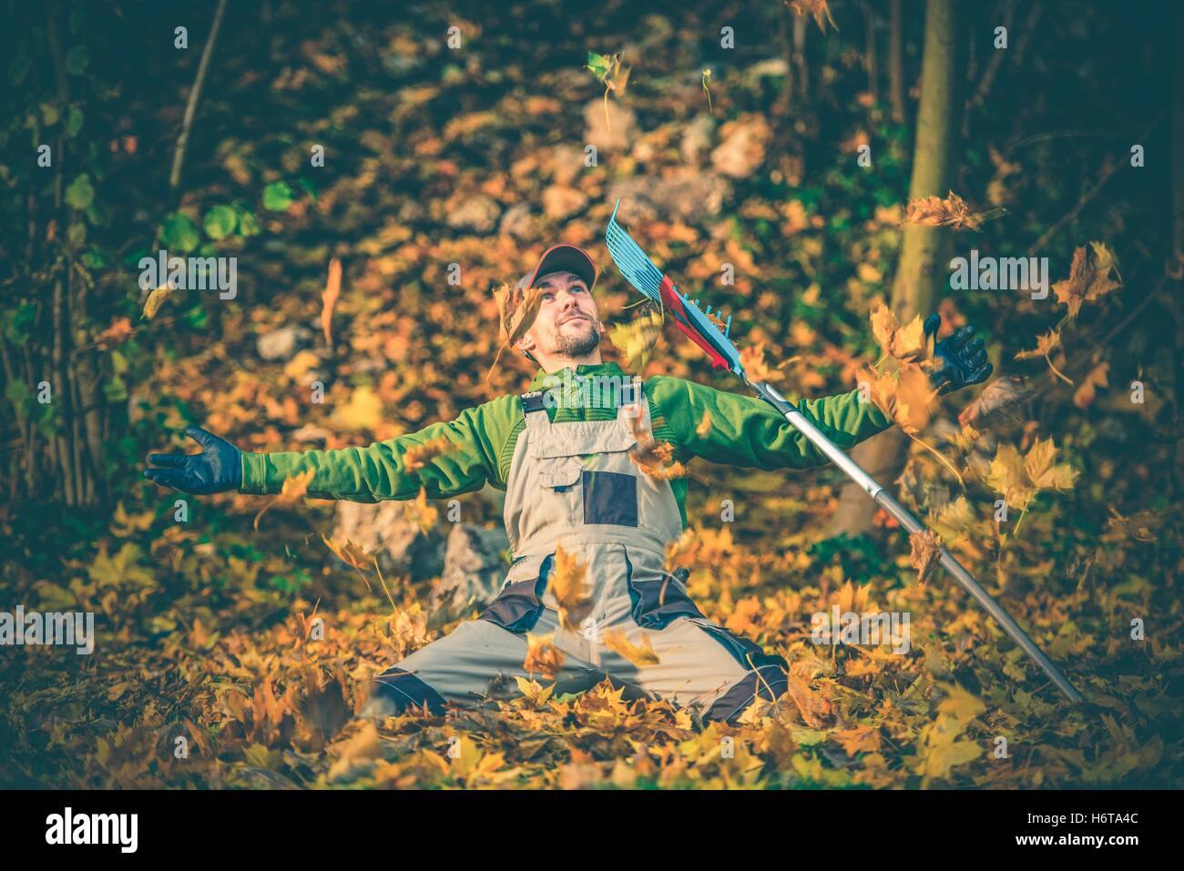 Gardener Welcome Fall Season Between Flying Colorful Leaves. Autumn Season Landscaping Concept. Happy Gardener with Rake. Stock Photo