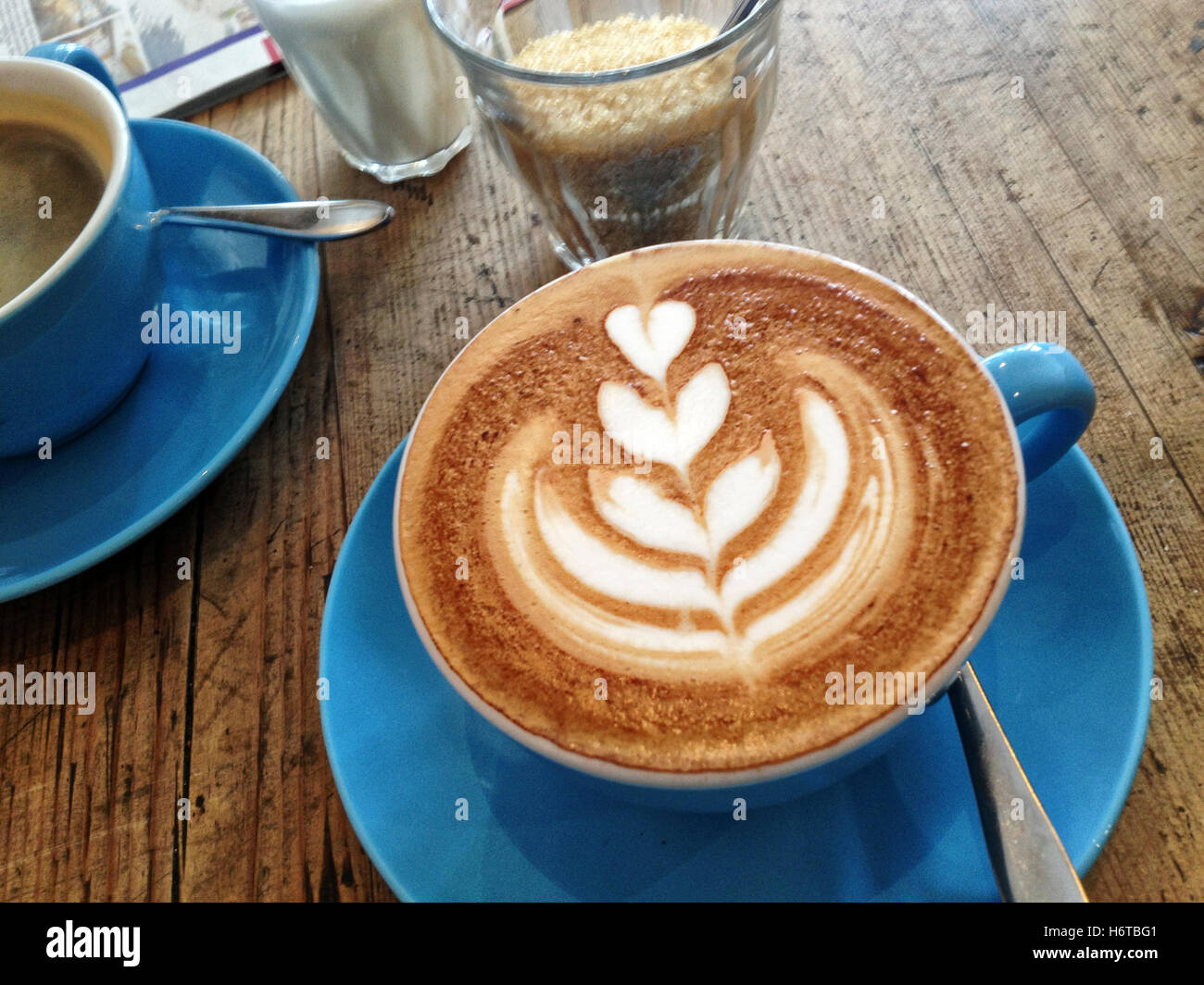 Stunning coffee art on top of a cappuccino in a blue cup on rough wooden table in an artisan coffee shop Stock Photo
