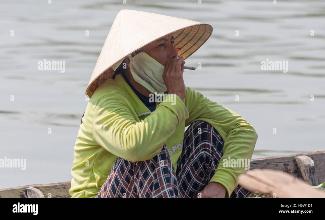 woman sitting boat smoking non la hat Hoi An, Vietnam Stock Photo