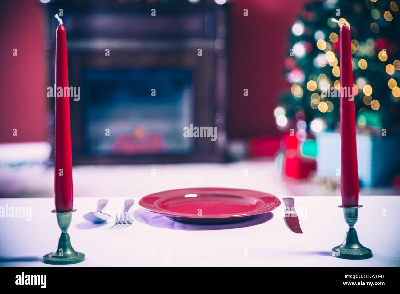 Beautifully laid new year table with red plates and Cutlery on a background of decorated room with Christmas tree and fireplace Stock Photo