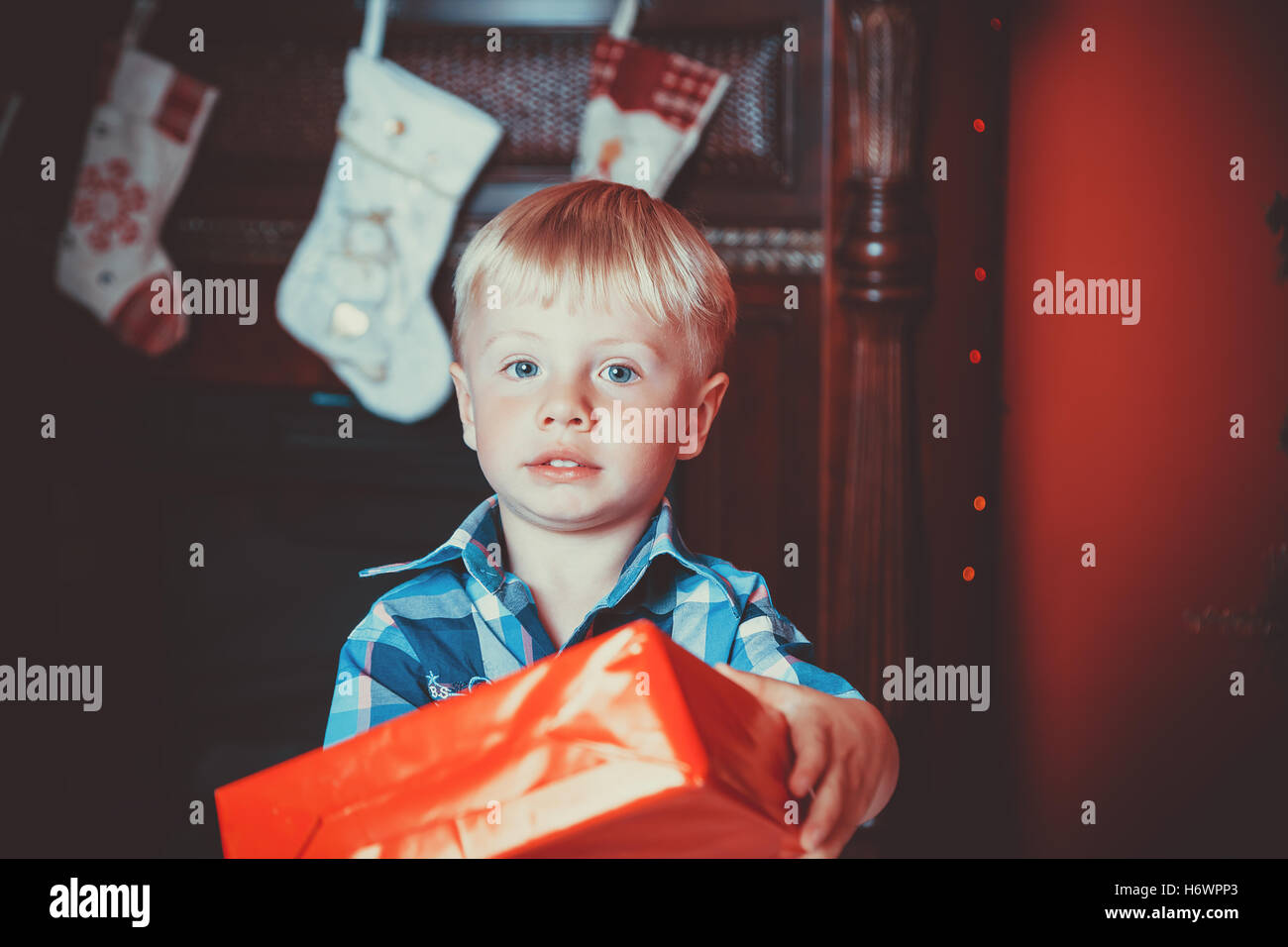 beautiful portrait of a little boy with a gift in hand in new year room with a Christmas tree. The idea for postcards. Soft focu Stock Photo
