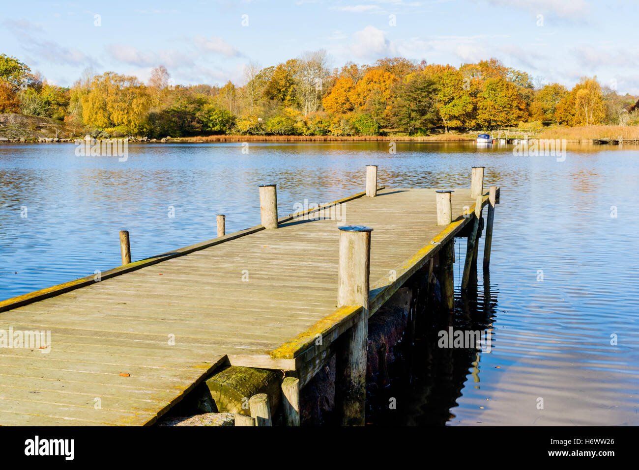 Wooden pier stretching out into the sea towards a small motorboat in the distance in fall. Jarnavik just outside Ronneby in Swed Stock Photo