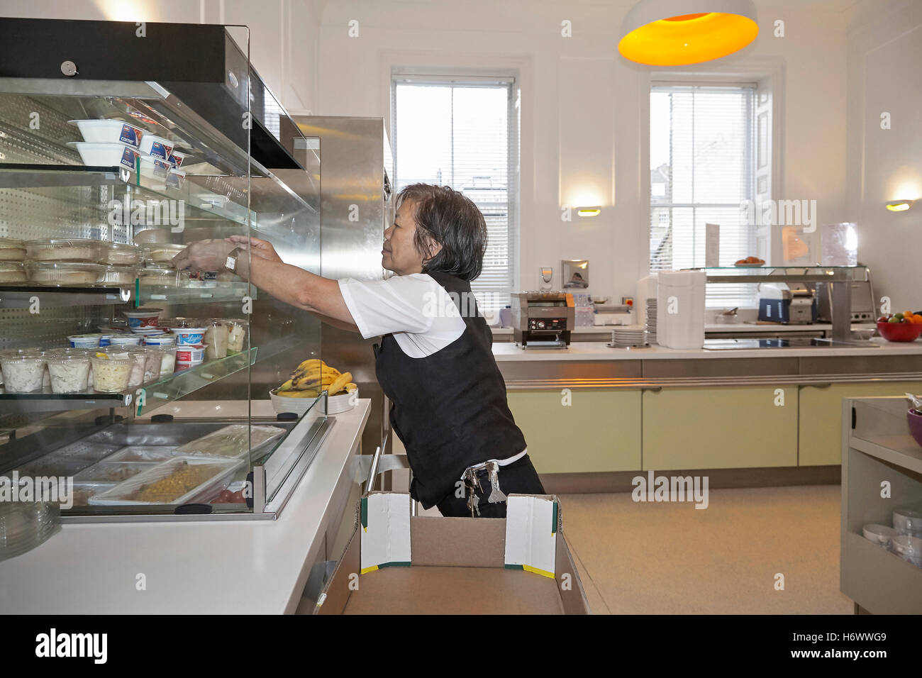 Kitchen worker, replenishing stock and tidying up in a works canteen
