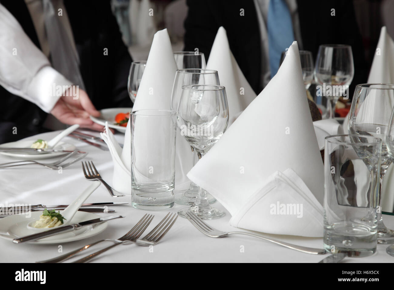Close-up of the hand of a waiter, serving on elegantly set table with two dressed-up persons. Stock Photo