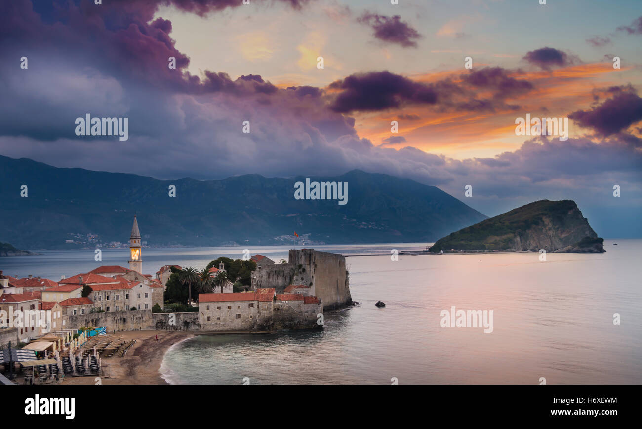 Sunrise over Budva old town with lit tower of Sv. Ivan church, old town's citadel and island Sv. Nikola to the right. Picturesqu Stock Photo