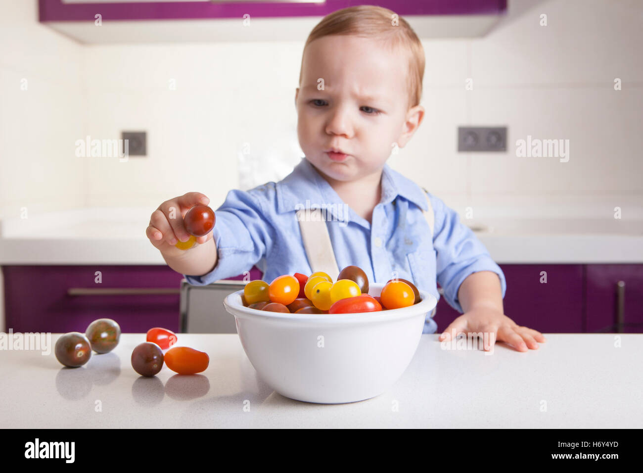 Baby boy holding a ripe colorful cherry tomatoe. Education on healthy nutrition for children concept Stock Photo