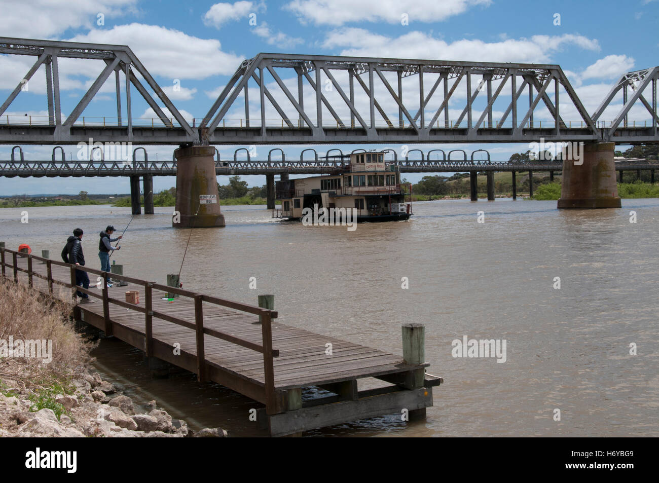 Men fishing as a restored paddlesteamer passes under road and rail bridges on River Murray at Murray Bridge, South Australia Stock Photo