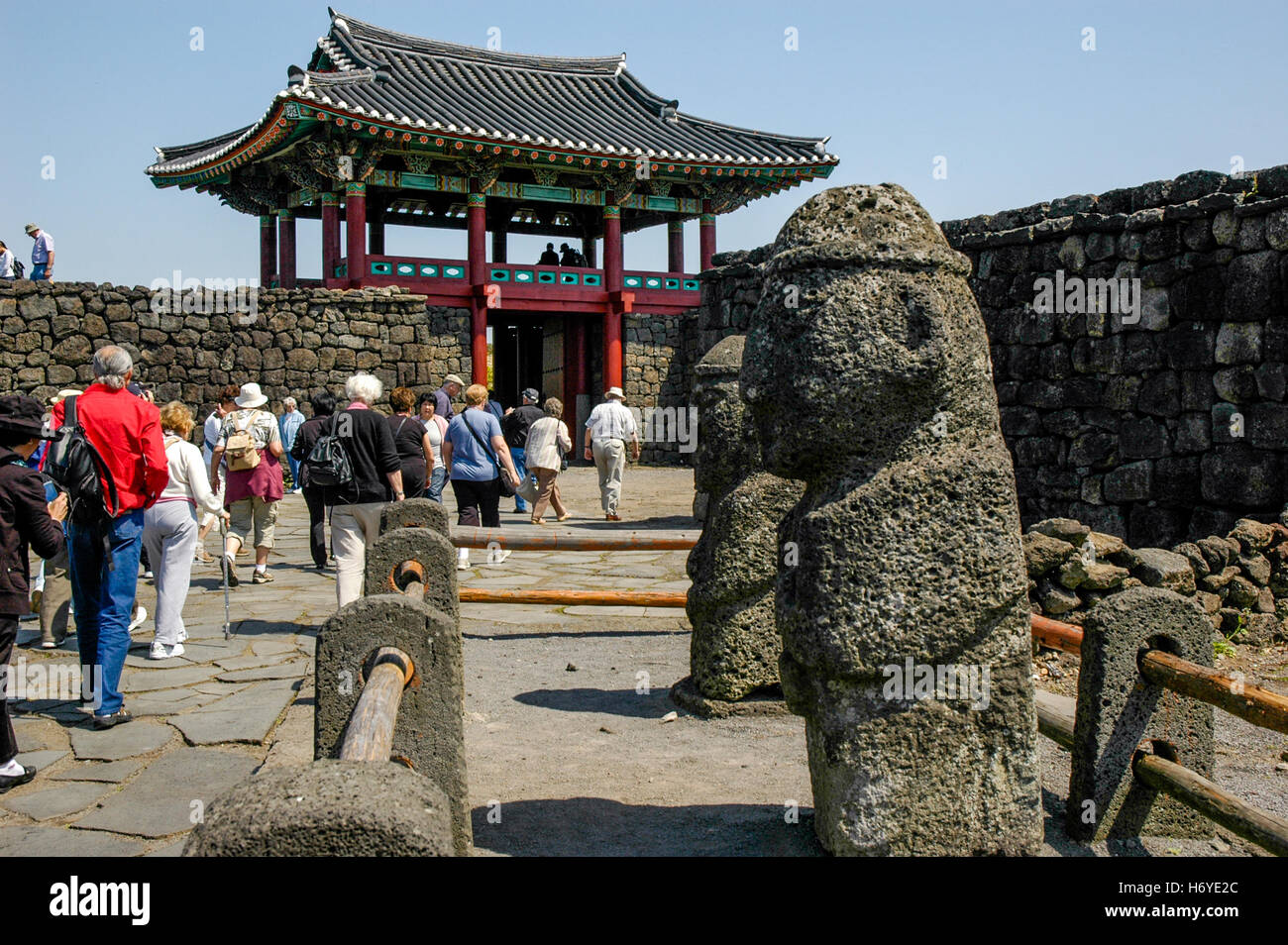 visitors walk past stone carvings at entrance gate of seongeup folk village. jeju (cheju). sth korea Stock Photo