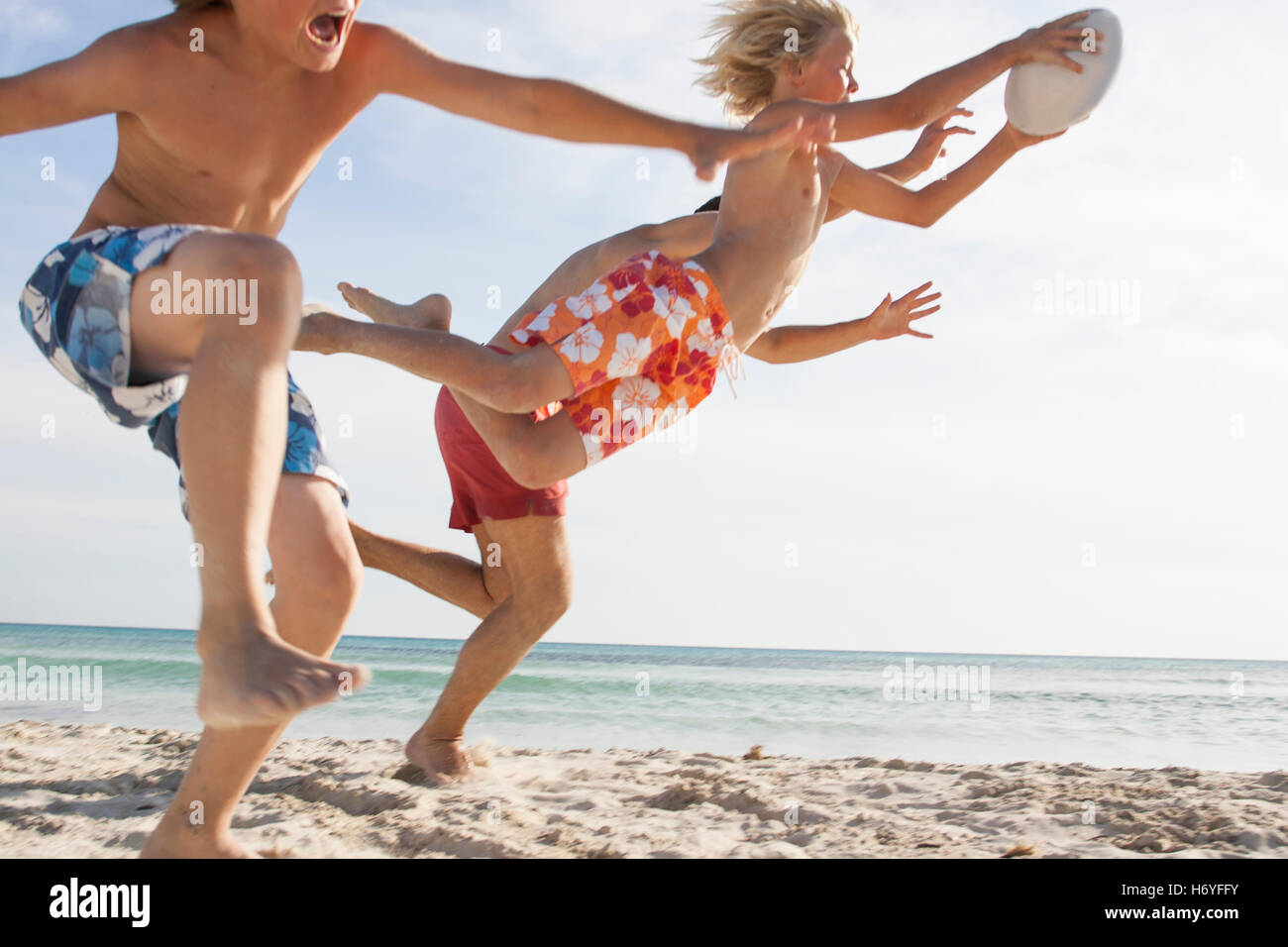 Boy and father running to reach brother with rugby ball on beach, Majorca, Spain Stock Photo