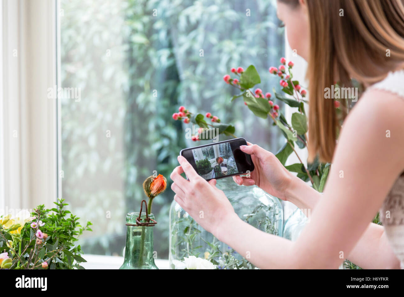 Over the shoulder view of woman using smartphone to take picture of flower in vase  Image downloaded by Hannah Zeffert at 13:44 Stock Photo