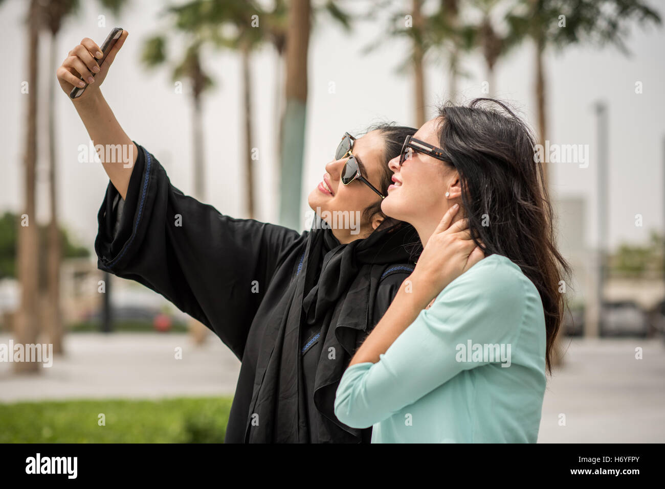 Young middle eastern woman wearing traditional clothing taking smartphone selfie with female friend, Dubai, United Arab Emirates Stock Photo