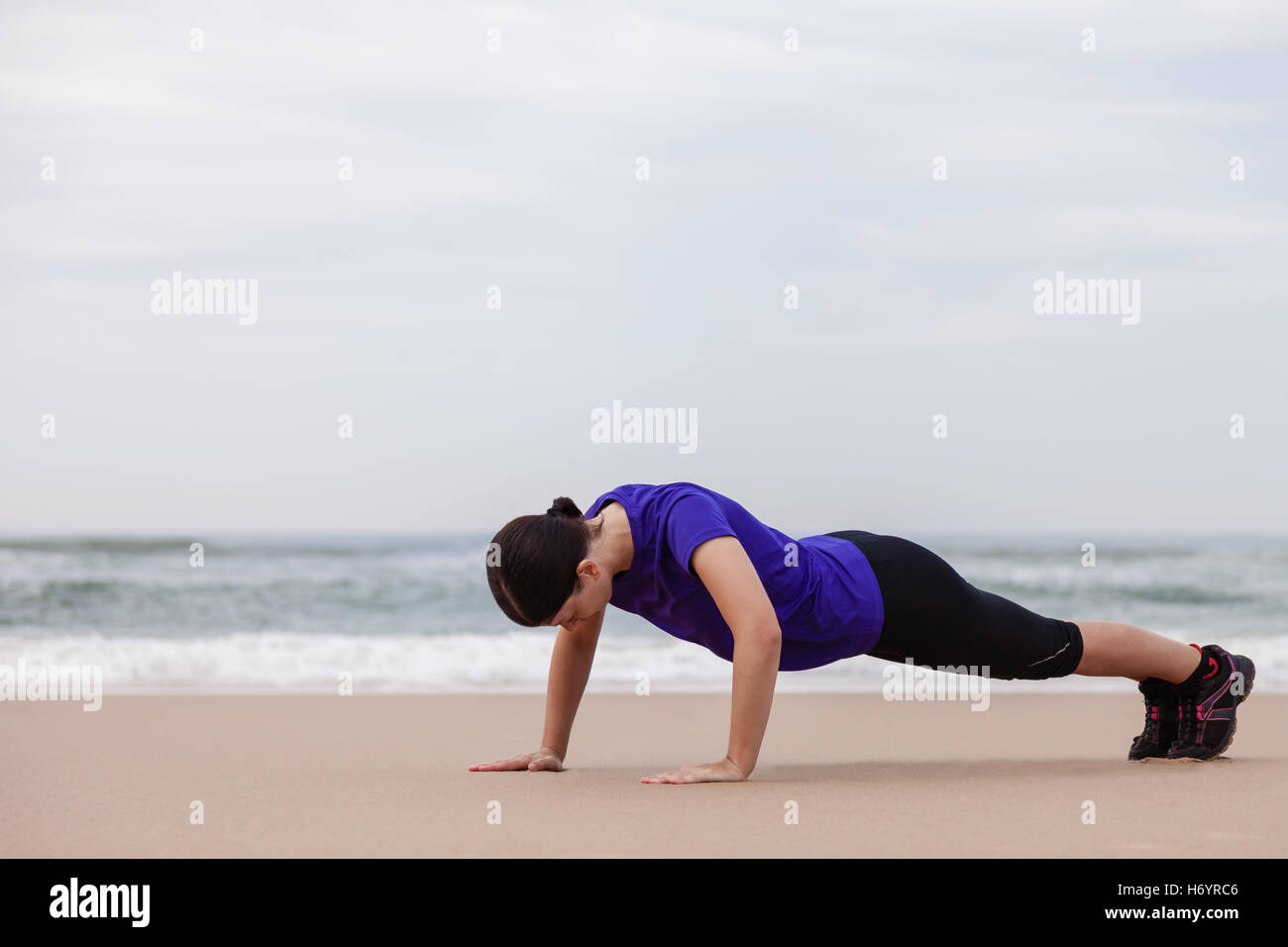 Female athlete executing push-ups at the beach on an Autumn day. Stock Photo