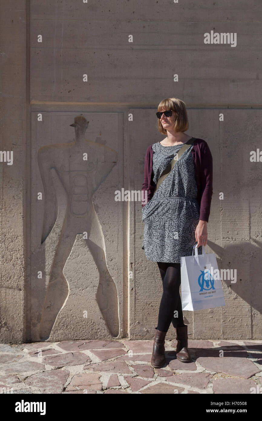 Woman with Olympique Marseille bag stands beside a human form at unite d'habitation, Marseille France Stock Photo