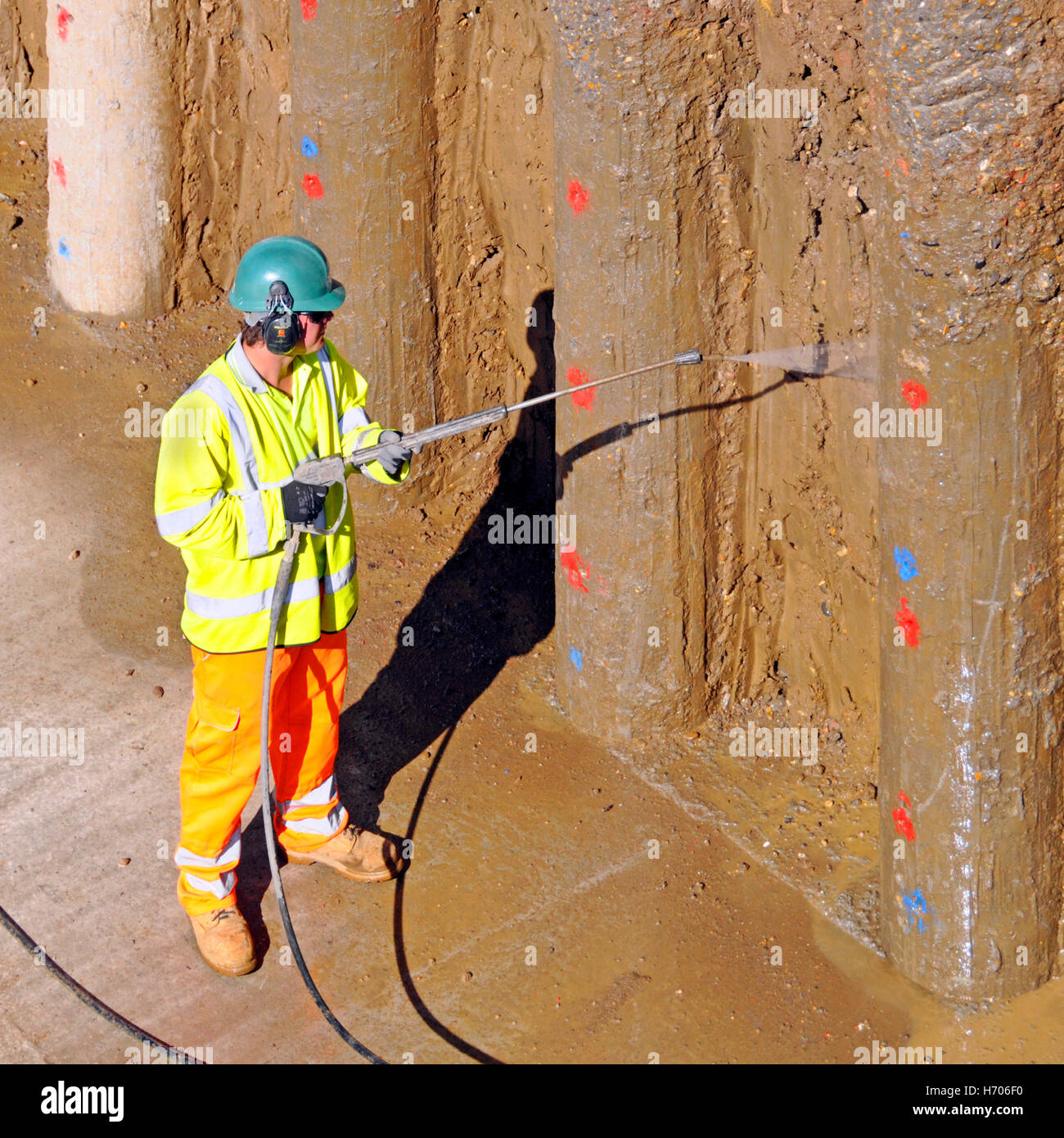 Retaining wall on building construction site worker high pressure water jet clean clay off new concrete piles M25 motorway widening Essex England UK Stock Photo