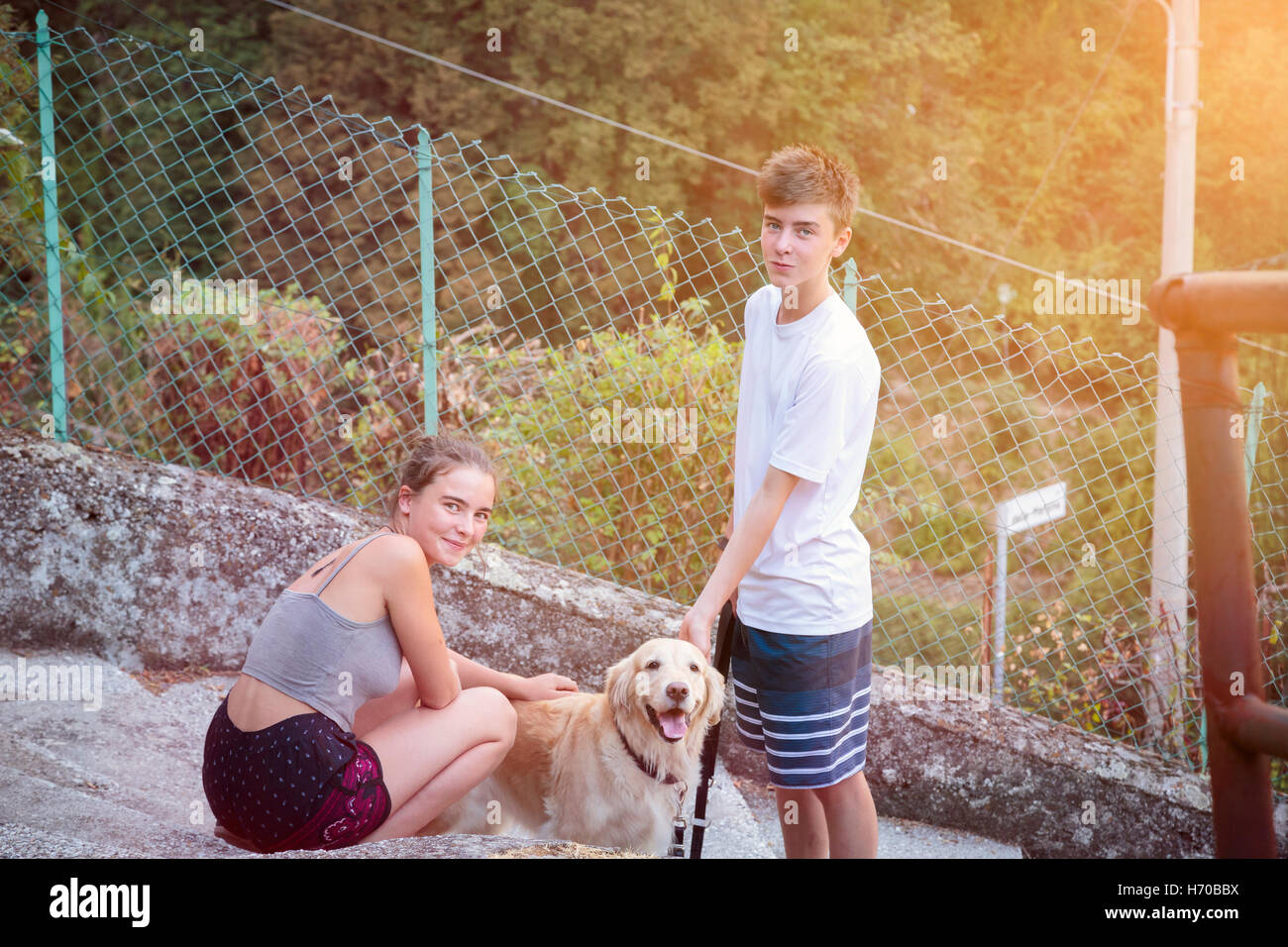 two smiling siblings walking with a dog Stock Photo - Alamy