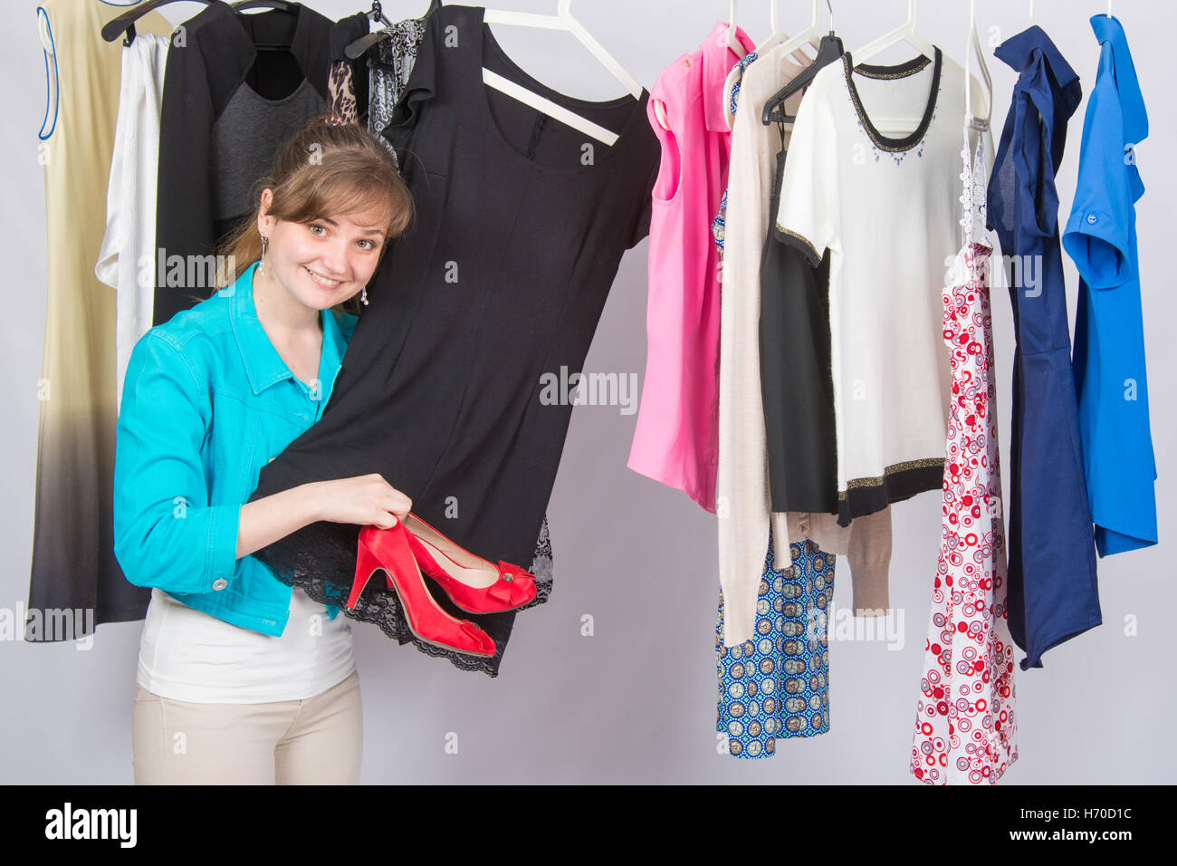 A young girl picked up the dress to the red high-heeled shoes thoughtfully chooses clothes in a wardrobe Stock Photo