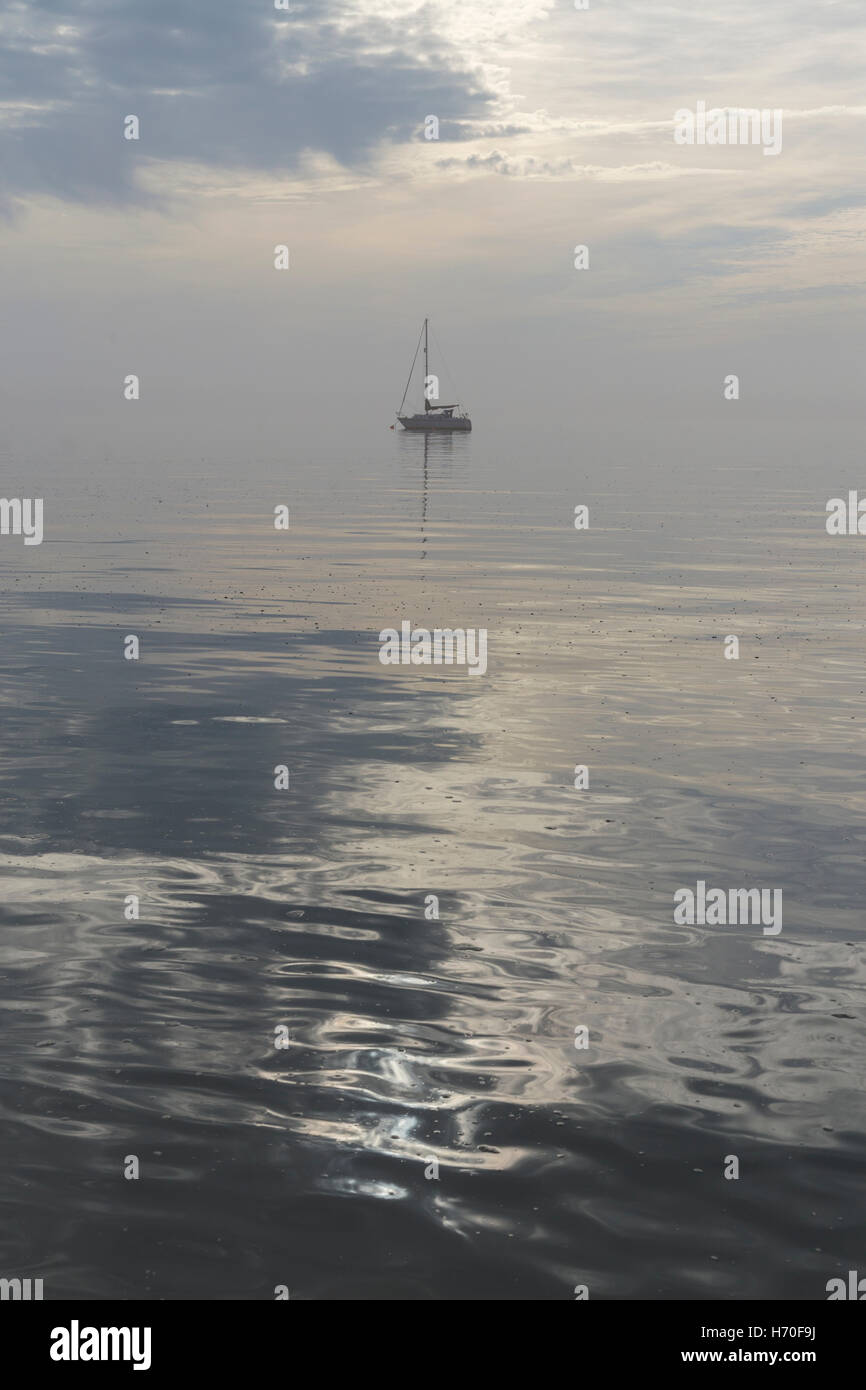 Calm and Misty Morning with Glass-like surface as Tide Rises with Yacht in Background Stock Photo