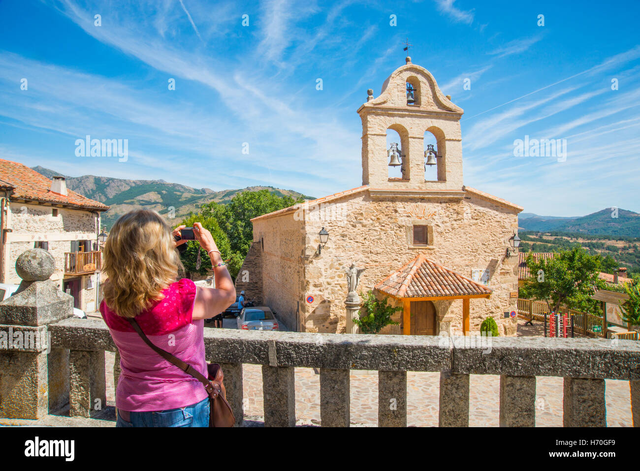 Woman taking photos from the viewpoint over the church and the Main Square. La Hiruela, Madrid province, Spain. Stock Photo