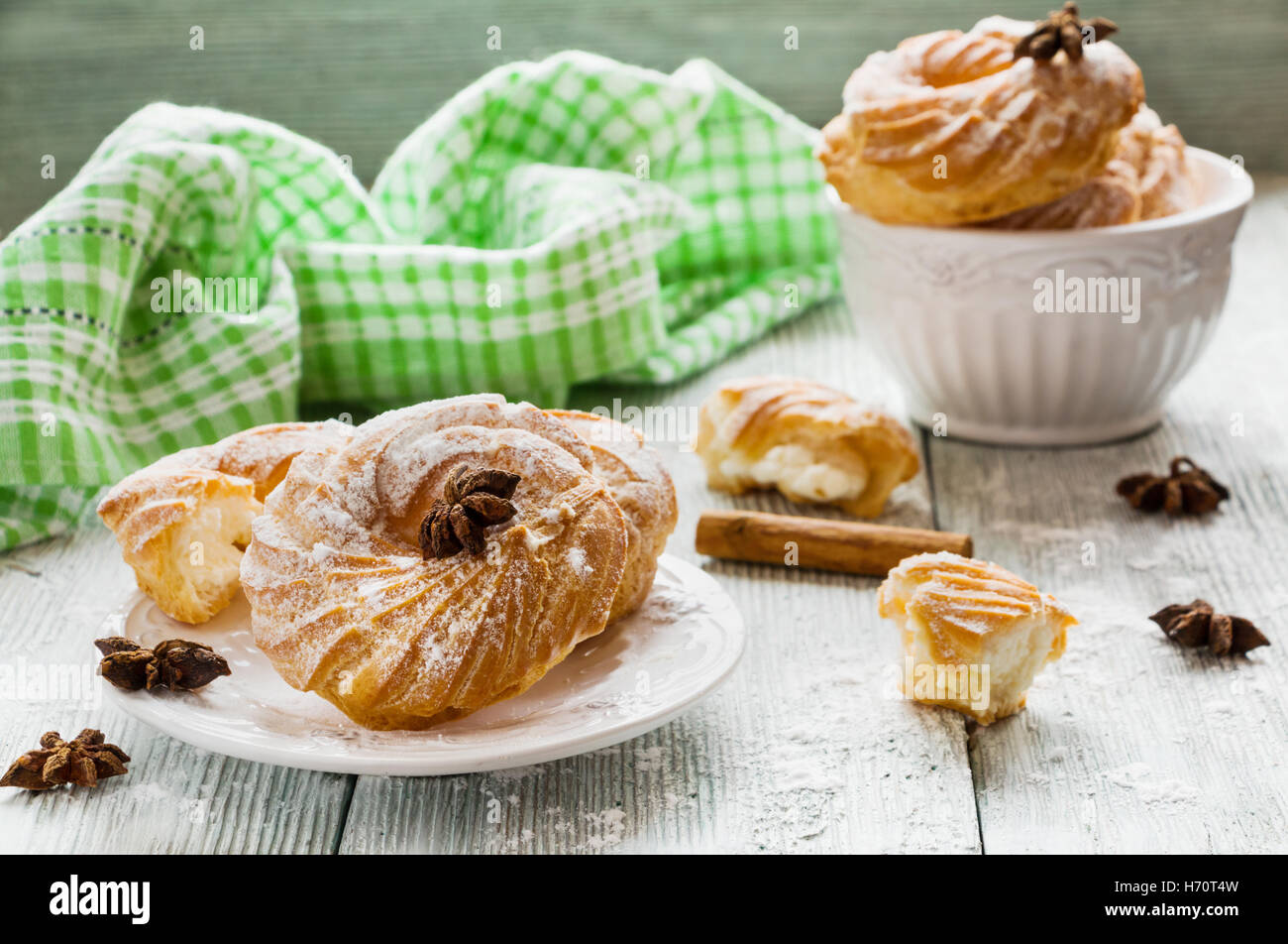 Round cakes with vanilla cream and powdered sugar on a wooden table, white vintage crockery. Stock Photo