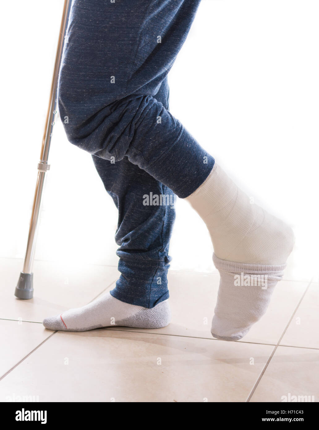 Young man with a broken ankle and a white leg cast with a sock to help keeping his toes warm, walking on crutches (isolated on w Stock Photo