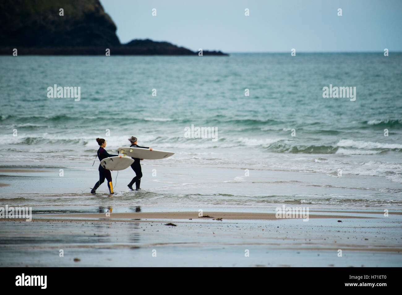 Two young woman wearing wet suits carrying their surfboards towards the sea at Hell's Mouth beach (Porth Neigwl), Lleyn Peninsula,  Gwynedd Wales UKWales UK October 2016 Stock Photo