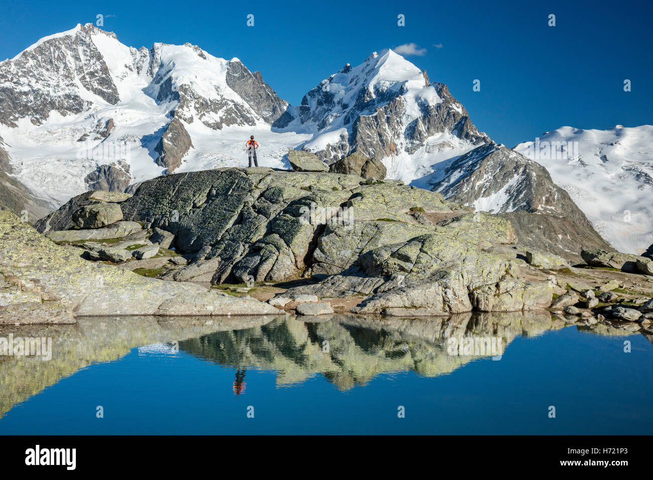 Reflection of hiker beneath Piz Bernina and Piz Rosbeg. Fuorcla Surlej, Silvaplana, Berniner Alps, Graubunden, Switzerland. Stock Photo