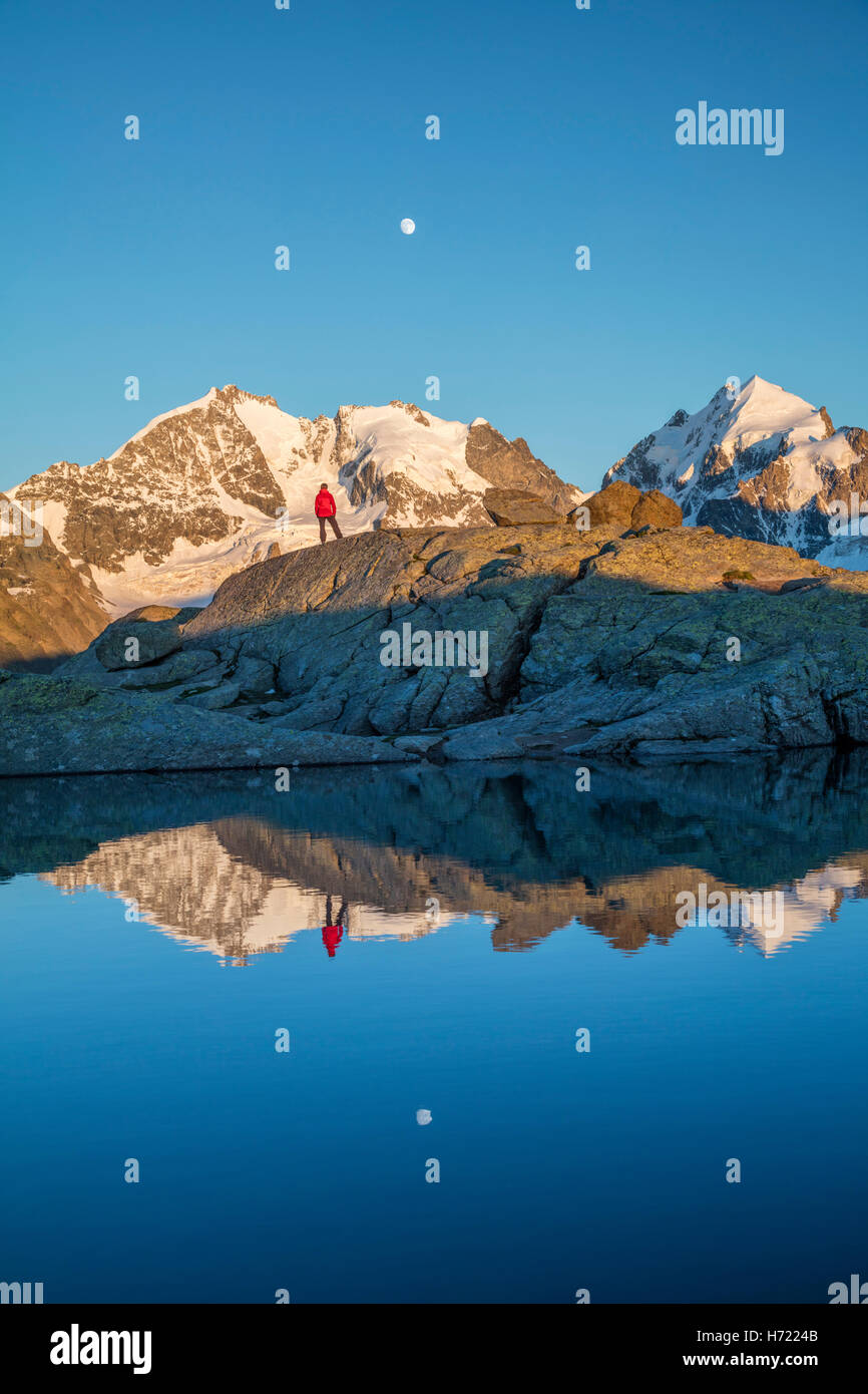 Reflection of hiker beneath Piz Bernina and Piz Rosbeg. Fuorcla Surlej, Silvaplana, Berniner Alps, Graubunden, Switzerland. Stock Photo