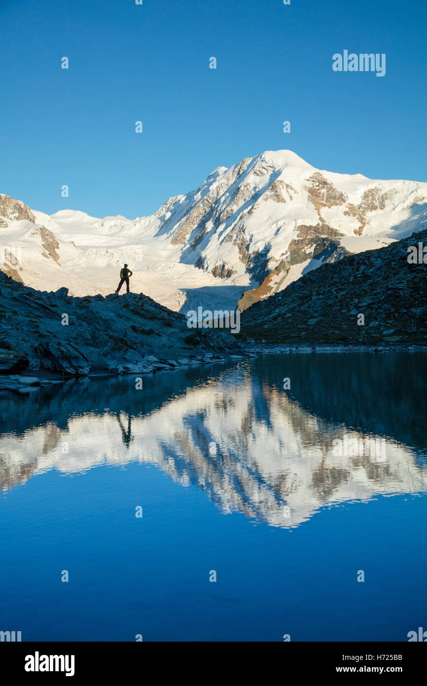 Hiker and Lyskamm reflected in the Riffelsee, Zermatt, Pennine Alps, Valais, Switzerland. Stock Photo