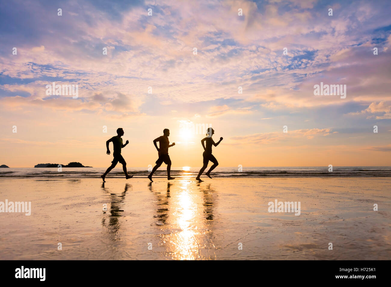 Group of three joggers running on a beach in summer at sunset - concept about healthy sportive lifestyle and community Stock Photo