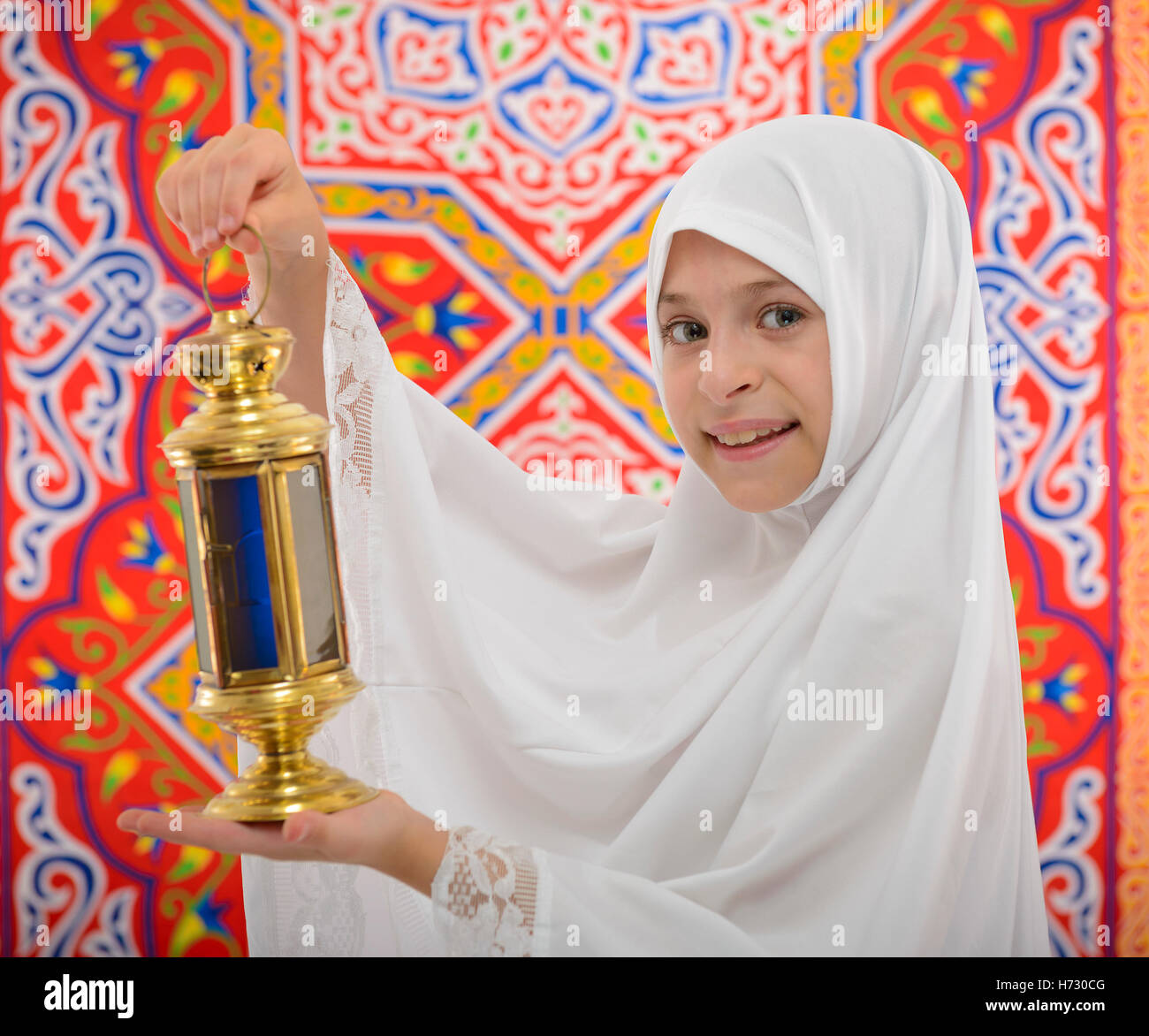 Happy Muslim Girl Holding Festive Ramadan Lantern over Ramadan Fabric Stock Photo