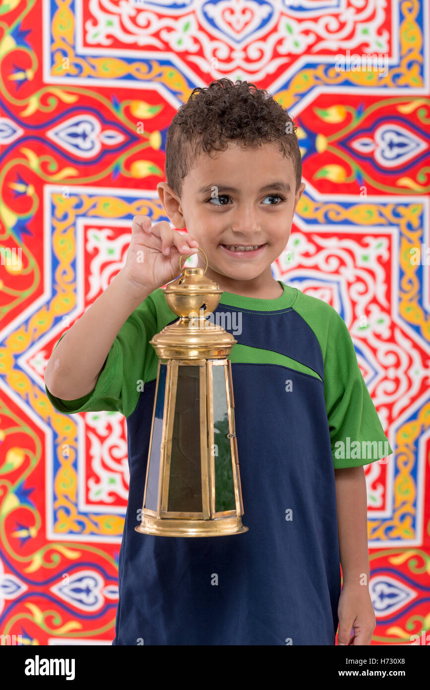 Adorable Young Boy Looking Away with Vintage Lantern over Festive Ramadan Fabric Stock Photo