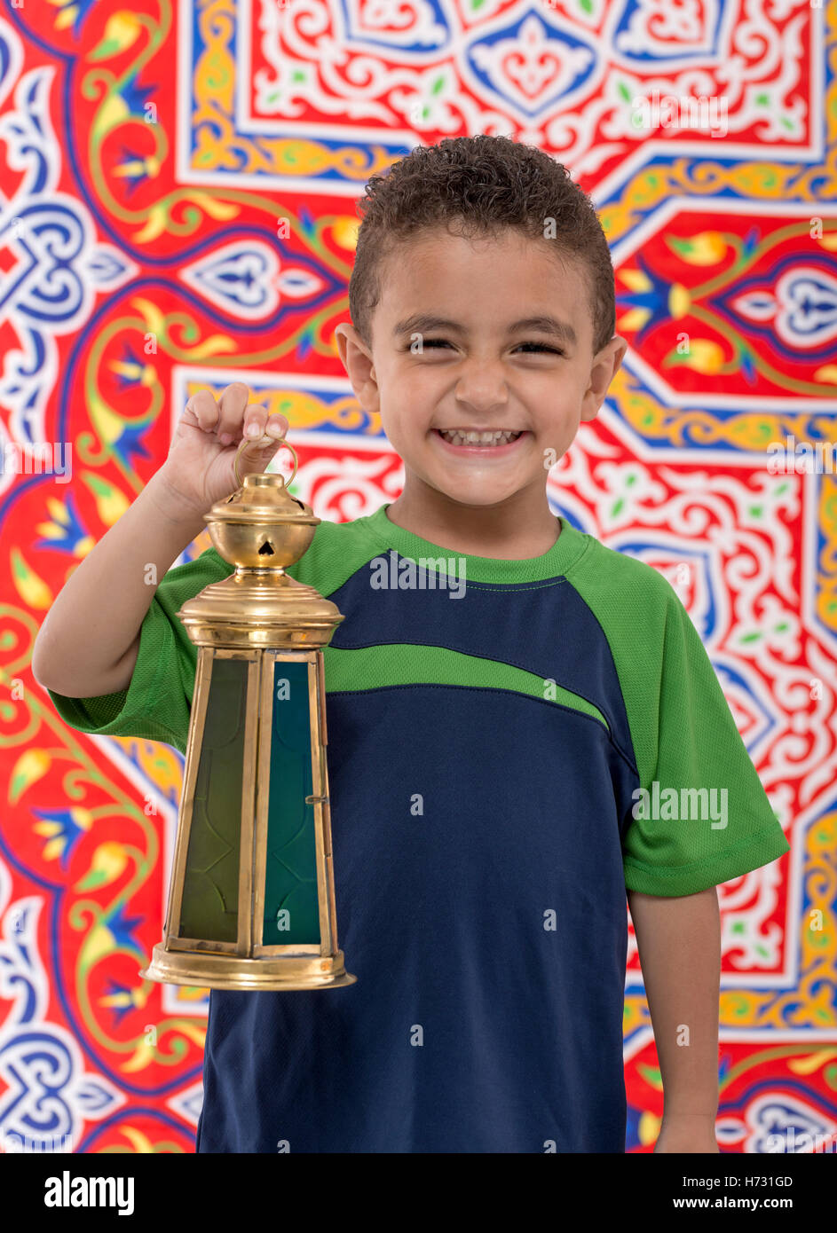 Adorable Smiling Young Boy with Vintage Lantern over Festive Ramadan Fabric Stock Photo