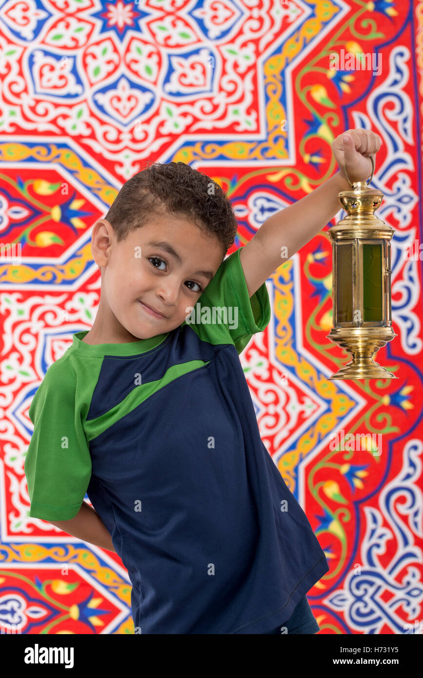 Adorable Young Boy with Vintage Lantern in Hand over Festive Ramadan Fabric Stock Photo