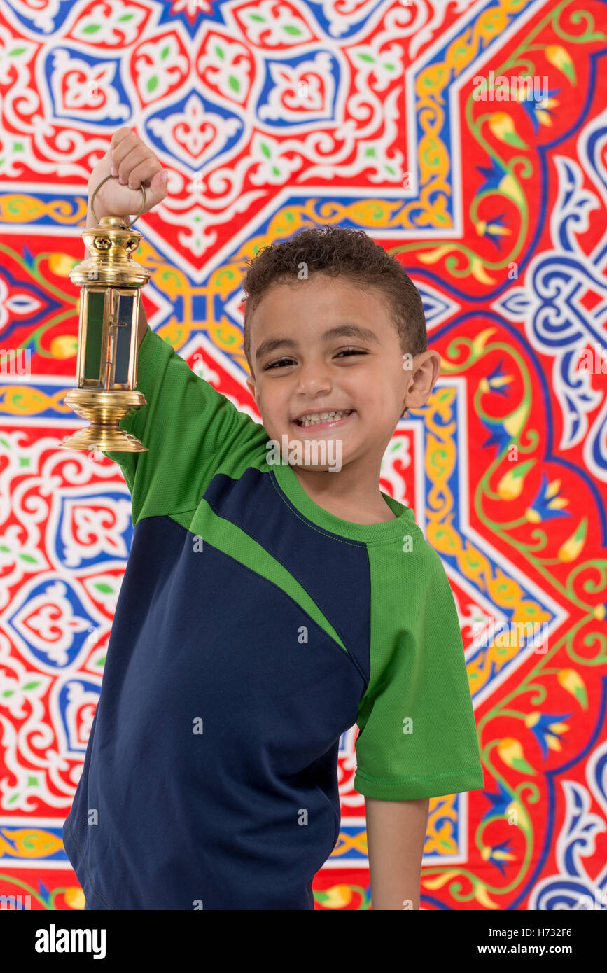 Smiling Young Boy with Vintage Lantern over Festive Ramadan Fabric Stock Photo