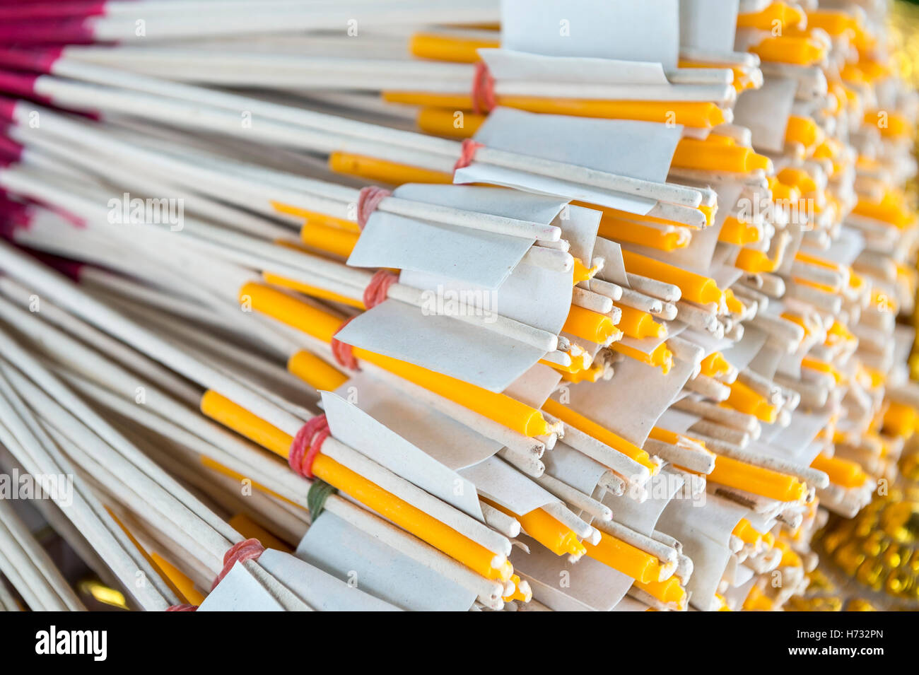 Bundle of red-tipped sticks of incense and yellow candles wrapped in white paper bundled and stacked in a Buddhist shrine Stock Photo