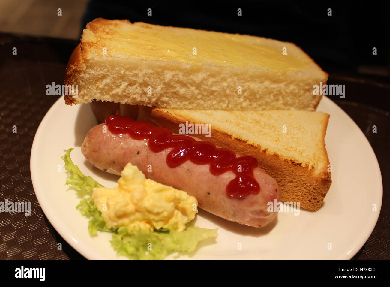 A freshly grilled hotdog with a stream of ketchup, butter toast bread