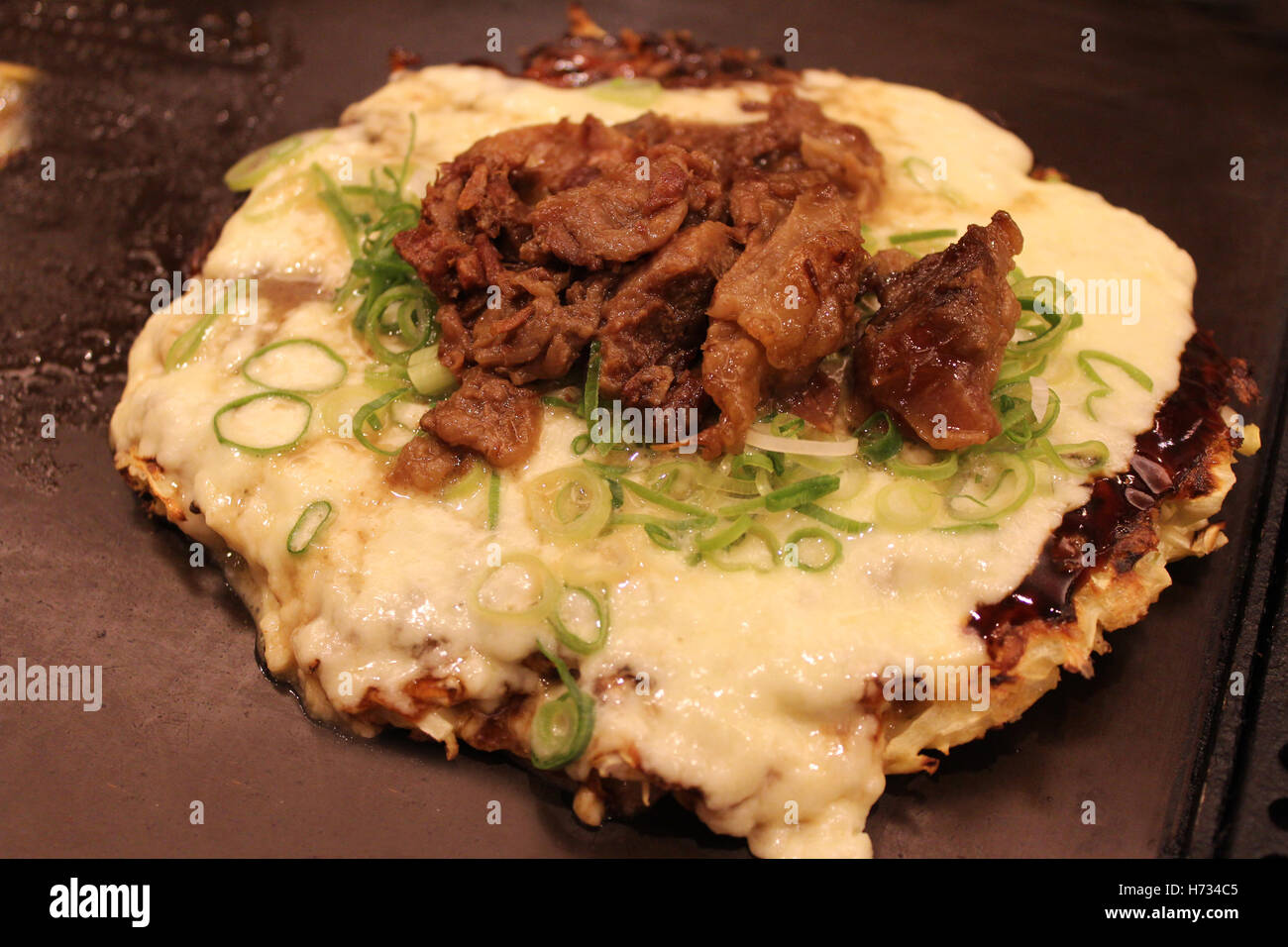 Okonomiyaki, Japanese Pizza topped with cheese, green onion and beef on the hot iron plate in Kyoto, Japan Stock Photo