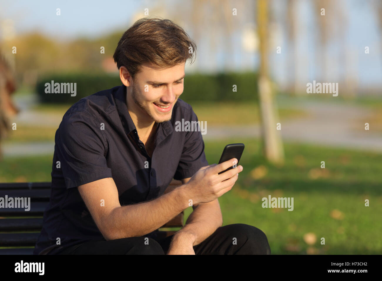 Man using a smartphone sitting on a bench in a park Stock Photo