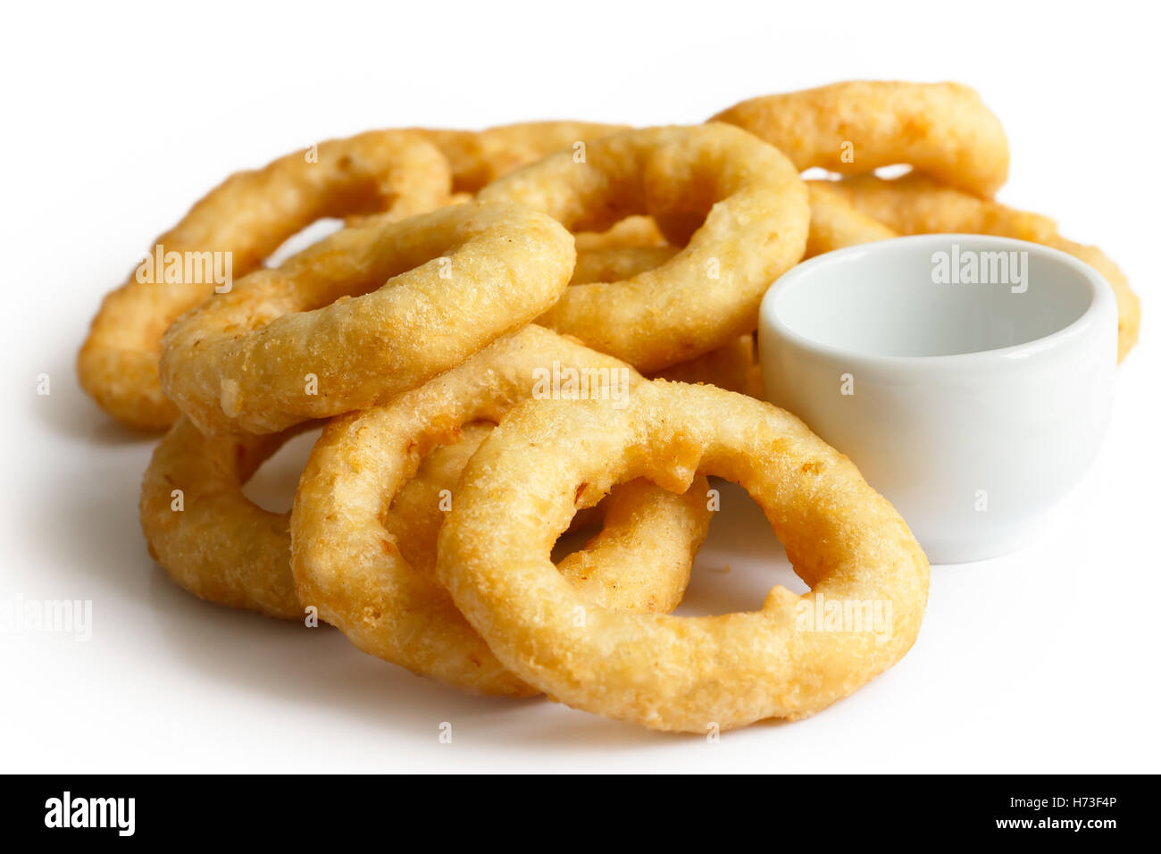 Heap of deep fried onion or calamari rings with dipping dish isolated on white. Stock Photo