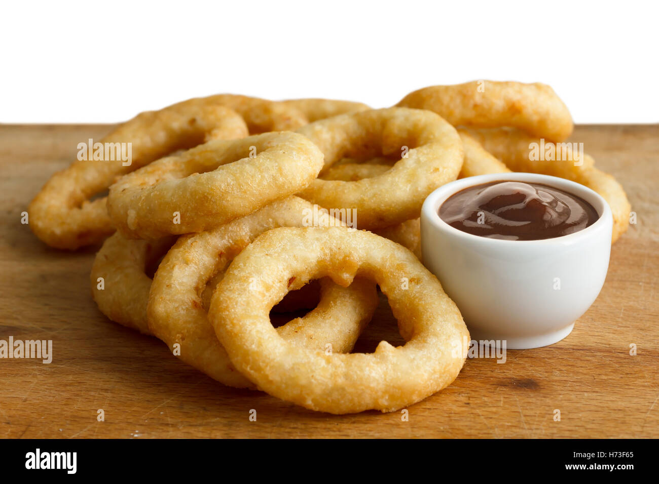Heap of deep fried onion or calamari rings with barbecue dip on wood board. Stock Photo