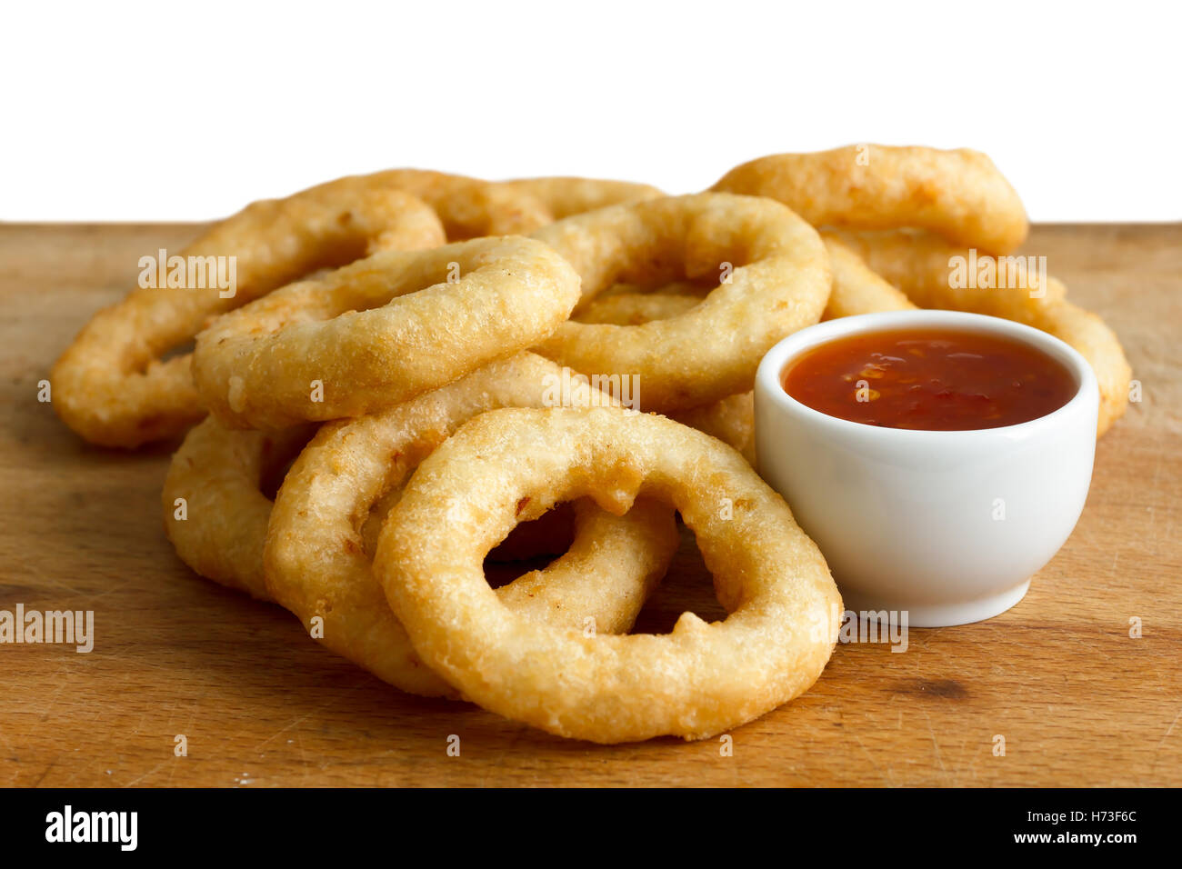 Heap of deep fried onion or calamari rings with chilli dip on wood board. Stock Photo