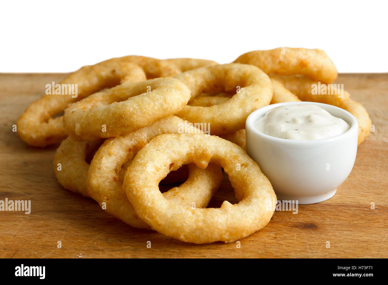 Heap of deep fried onion or calamari rings with garlic mayonnaise dip on wood board. Stock Photo